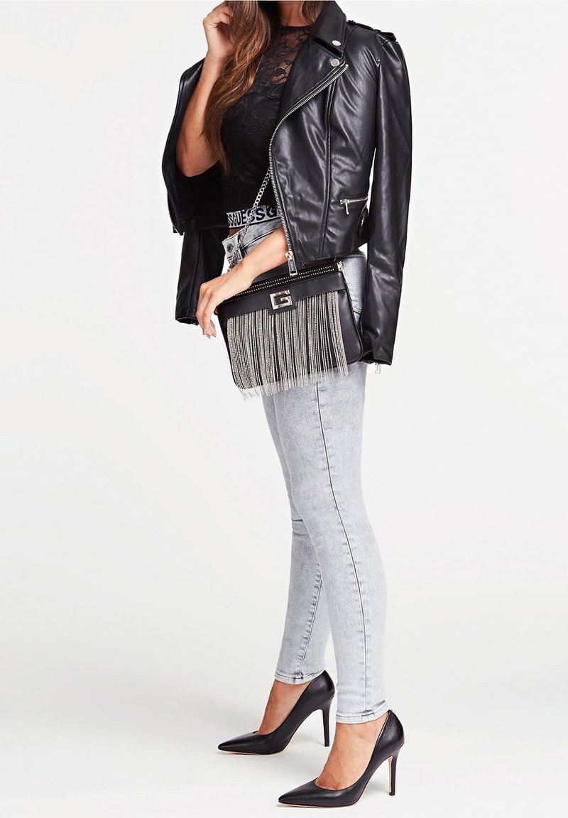 Musta nahkatakki moottoripyöräilijälle mustan pitsipaidan päällä, harmaat tiukat farkut ja mustat korkokengät; olkalaukku, jossa on koristeellista fringedetailia.