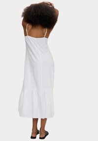 Weißes, ärmelloses Kleid mit gestuftem Saum und dünnen Trägern, aus leichtem Stoff, mit schmalem Schnitt und subtiler Textur.