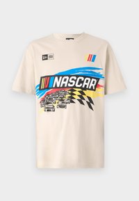 T-shirt en coton beige avec un graphique coloré de NASCAR représentant des voitures de course, des drapeaux à damier et une lettrage audacieux. Manches courtes, col rond.