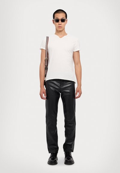 Witte V-hals t-shirt, zwarte leren broek, zwarte schoenen, zonnebril en een schoudertas met een meerkleurige gestreepte band.
