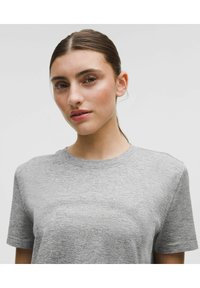 Grå kortärmad t-shirt i ett texturerat tyg med rund halslinning och diskreta designdetaljer längs bröstet.