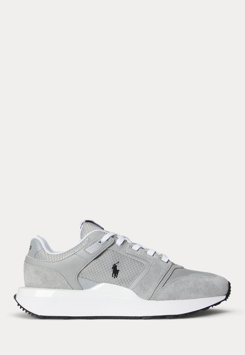 Baskets de sport grises et blanches avec panneaux en mesh et en daim, lacets blancs et logo noir sur le côté, présentées sur un fond uni.