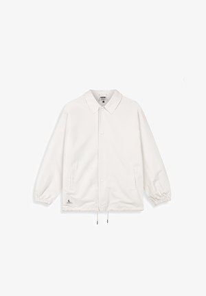 Biała lekka kurtka z kołnierzem, zatrzaskami, elastycznymi mankietami i ściągaczem u dołu. Posiada dwie boczne kieszenie oraz metkę z logo.