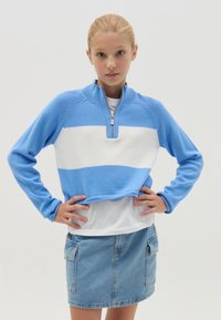 Pullover corto a righe blu e bianche con colletto a zip quarti, abbinato a una gonna in denim con tasche laterali. Texture della maglia liscia.