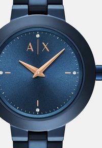 Krožna modra kovinska ura z teksturirano številčnico, rožnato zlato uro in minuto ter dvema diamantoma, in eleganten modri dizajn zapestnice.