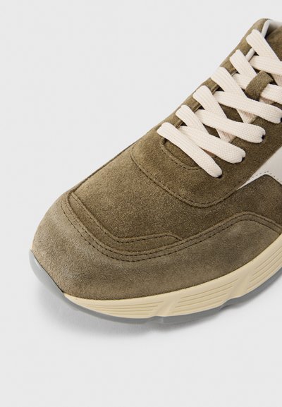 Αθλητικό παπούτσι από σουέτ σε ελιά πράσινο με μπεζ λεπτομέρειες, με υφασμένα πάνω μέρος, στρογγυλή μύτη και κρεμ κορδόνια. Μαλακό, ανθεκτικό υλικό με αθλητική σχεδίαση.