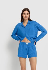 Blårandig pyjamasset med en knapp-up skjorta med ficka och shorts med elastisk midja. Tillverkad av lättviktig tyg med en avslappnad passform.