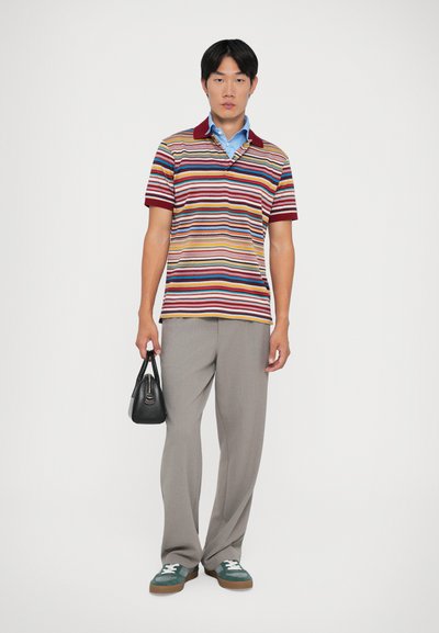 Polo a righe di colori diversi con colletto bordeaux, pantaloni grigi a vita alta, borsa nera e sneakers verdi con lacci bianchi.