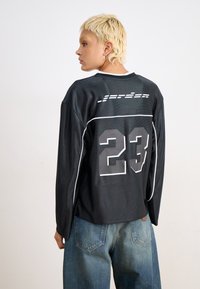 Svart langermet trøye med grått nummer "23" og horisontale striper. Lett stoff med kontrasterende hvit piping langs sømmene.