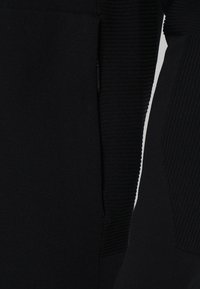 Detailní záběr na černou texturovanou látku s žebrovanými pletenými vzory na rukávu a bočním panelu oděvu.