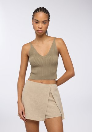 Top corto a coste oliva con scollatura a V profonda, abbinato a una gonna avvolgente beige con finitura testurizzata e spacco laterale.