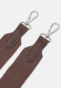 Ruskea kangashihna, jossa metalliset kääntyvät lenkit. Ompeleissa vahvistettuja kiinnityspisteitä ja teksturoitu pinta. Kestävä ja toimiva muotoilu.