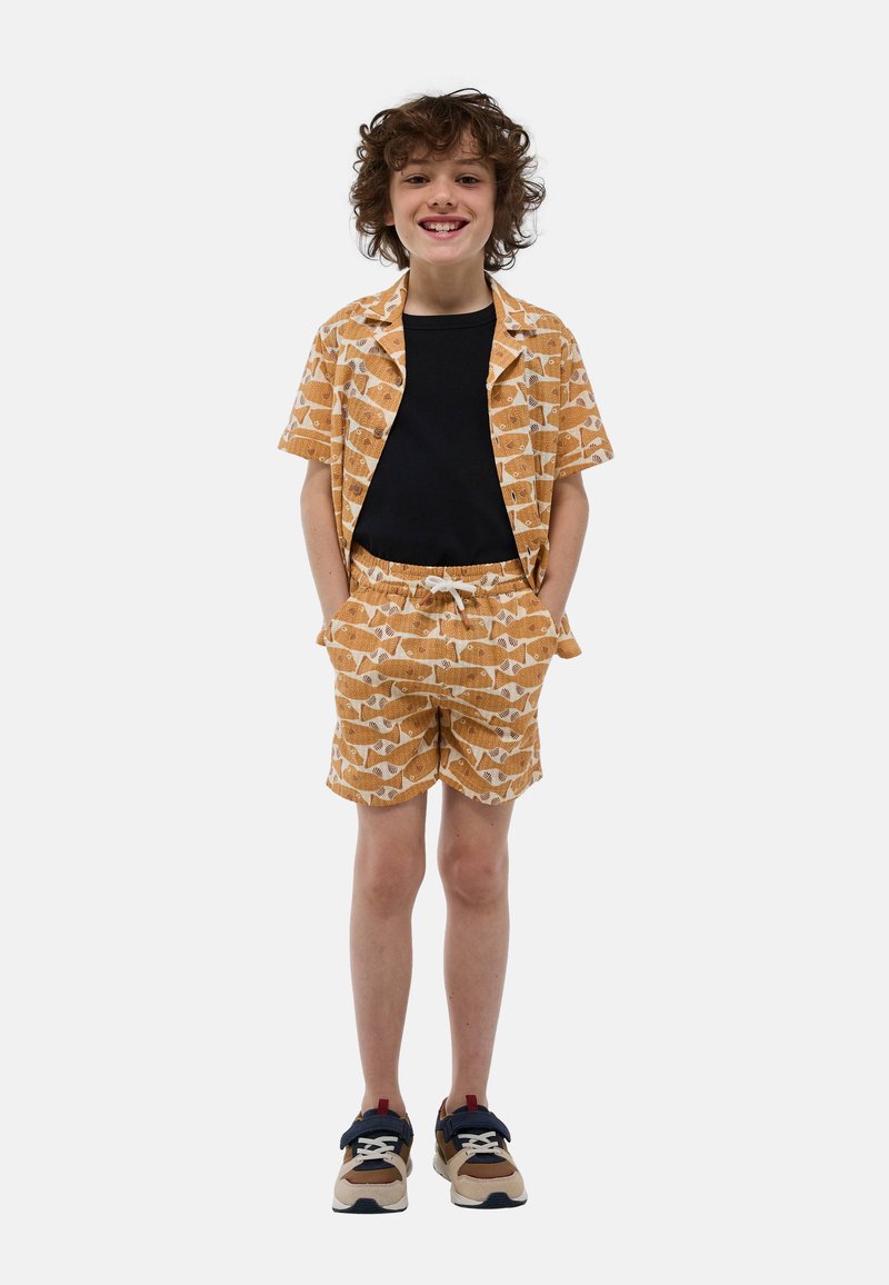 Chemise orange à manches courtes et shorts assortis avec un motif de poissons, associés à une chemise noire et des baskets multicolores.