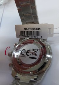 Baksidan av ett armbandsur i rostfritt stål, cirkulär form, med ett skyddande klistermärke, inklusive en streckkodsetikett och en vattentålig etikett.