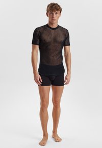 Sort mesh t-shirt med korte ærmer, ribbet krave og tætsiddende design, parret med sorte boxershorts. Meshstrukturen er fremtrædende.