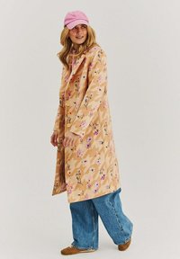 Béžový deštník s květinovým vzorem a růžovými akcenty, s přizpůsobeným střihem, v kombinaci s volnými modrými džíny a růžovou kšiltovkou.