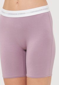 Lyslilla shorts med en glat tekstur og en hvid elastisk talje. Taljen har teksten "COPENHAGEN STUDIOS" trykt.
