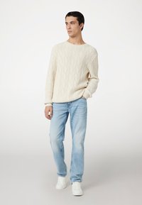Maglione lavorato a maglia avorio con scollo a giro, abbinato a jeans azzurri e sneakers bianche. Il maglione presenta polsini e orlo a coste.
