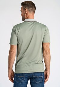 Ljusgrön polo med kort ärm och grå krage, med en slät textur och en avslappnad passform, tillsammans med blå jeans.