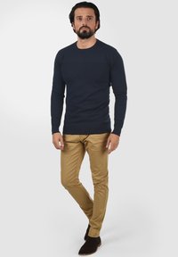 Marineblaues Langarmshirt aus strukturiertem Strick, kombiniert mit schmal geschnittenen khakifarbenen Hosen und braunen Wildleder-Ankle-Boots. Einfaches, lässiges Ensemble.