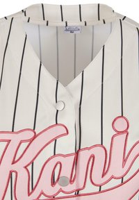 Hvit baseballtrøye med svarte vertikale striper, rosa brodert "Kani"-logo, V-halsdesign og metallknappdetalj foran.