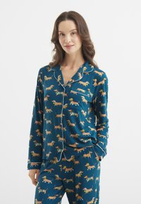 Passendes Pyjama-Set aus weichem, teal-farbenem Stoff mit einem wiederholten Hunde-Muster. Beinhaltet ein langärmliges Oberteil mit Tasche und Knopfverschluss.