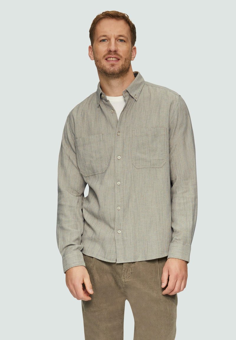 Grijs herringbone-patroon overhemd met knopen, voorzien van twee borstzakken en een kraag. Draag het over een wit t-shirt, gecombineerd met ribfluwelen broek.
