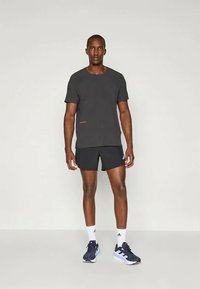 Melna T-krekls ar īsām piedurknēm un sarkanu akcentu malā, kopā ar melniem šortiem un tumši ziliem sporta apaviem.