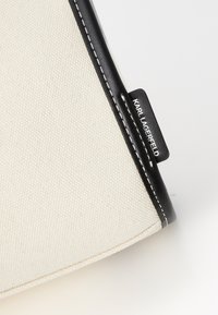 Sac en toile avec un corps blanc, des accents en cuir noir, des coutures blanches et une petite étiquette noire avec le texte "KARL LAGERFELD".