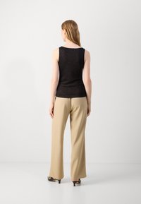 Black sleeveless top with a subtle shine, paired with beige wide-leg trousers, seen from the back. Flat-heeled shoes complete the outfit.