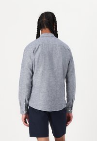 Langarm overhemd met knopen in een lichte blauwe gemêleerde stof. Heeft een standaardkraag, manchet met één knoop en een relaxte pasvorm.