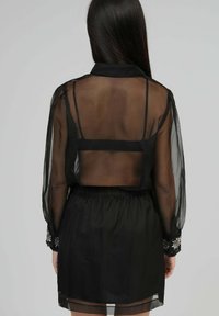 Robe noire transparente avec des manches longues, taille élastique, broderie florale sur les poignets, détail du dos dénudé et bretelles réglables.