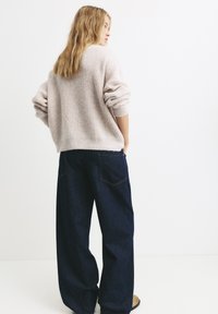 Helle rosa gestrickter Pullover mit umgeschlagenen Ärmeln, kombiniert mit weit geschnittenen dunkelblauen Denim-Jeans. Sichtbare Gesäßtaschen an den Jeans. Schlichtes Design.