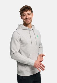 Ljusgrå huvtröja med framficka, dragsko i luvan och grön logodetalj på bröstet. Tillverkad av mjukt tyg med ribbade muddar.