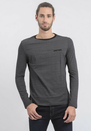 Chemise grise à manches longues avec une finition texturée, dotée d'un col noir et d'une petite poche accentuée d'un bouton marron.