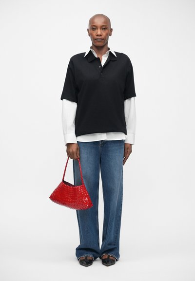 Polo nero sopra una camicia bianca con colletto, jeans blu a gamba larga e una piccola borsa intrecciata rossa. Scarpe nere con dettagli decorativi sulla superficie.