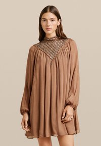 Vestido marrón de manga larga con diseño plisado y acentos de malla con cuentas. Cuello alto y corte holgado, hecho de una tela ligera y texturizada.