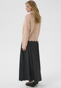 Suéter de punto rosa claro con un dobladillo ondulado, combinado con una falda larga de color gris oscuro y zapatos negros. Textura suave y ajuste relajado.