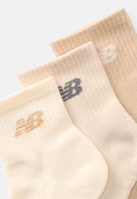 Drei Paare von beige und cremefarbenen gerippten Socken mit gestickten "NB"-Logos in verschiedenen Schattierungen, die sich überlappend auf einem weißen Hintergrund anordnen.