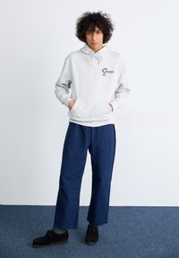 Light gray hoodie with a front pocket and black logo, paired with navy blue wide-leg pants and black shoes. Smooth texture, casual design.
