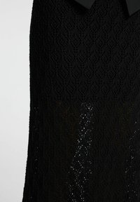 Sort blondekjole med et struktureret diamantmønster, med gennemsigtige områder der afslører en subtil glitreffekt i kanten.