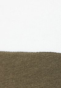 Bomullsmixat tyg med en krämfärgad övre del och en olivgrön strukturerad nedre del med ribbat stickat avslut.