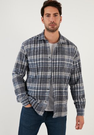 Camisa a cuadros azul y blanca de tejido texturizado, con cierre de botones en la parte delantera, un cuello clásico y mangas largas, usada sobre una camiseta gris.