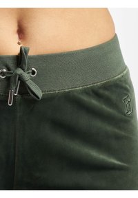 Gröna velour sweatpants med en texturerad midja, dragkedjeslutning och liten broderad logotyp på sidan.