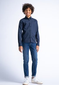 Camicetta blu navy con colletto, abbinata a jeans blu e sneaker bianche. La camicetta presenta un tessuto texturizzato e una linea dritta.