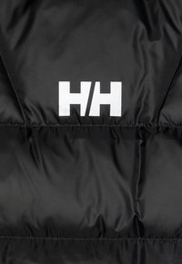 Chaqueta de plumas negra con superficie brillante, que presenta un prominente logo blanco "HH" y una forma cuadrada. Tejido texturizado con costuras cosidas.