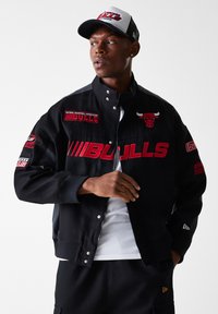 Black jacket with red "BULLS" lettering, Chicago Bulls logo, and various patches. Snap closure, ribbed cuffs, and contrasting sleeves.