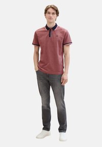 Rød polo skjorte med marineblå krave og striber, stylet med mørke jeans og hvide sneakers. Korte ærmer og broderet logo på brystet.