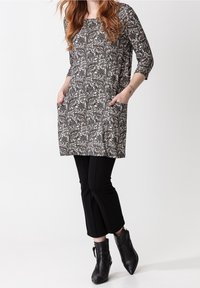 Tunika s paisley vzorem v černobílém provedení, s rukávy ke třetině, se bočními kapsami, kombinovaná s černými zkrácenými kalhotami a kotníkovými botami.