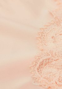 Jasnopomarańczowa tkanina z misternym koronkowym wykończeniem wzdłuż jednego brzegu, ozdobiona kwiatowymi wzorami i miękką, gładką teksturą.